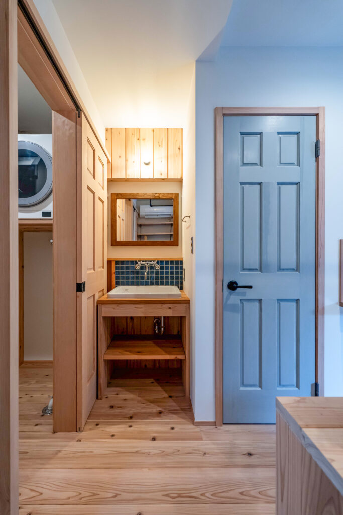 狭小住宅の家族クローゼットと水回り。シンプソンの木製ドアのトイレとタイル張りの造作洗面が横並びになっている。